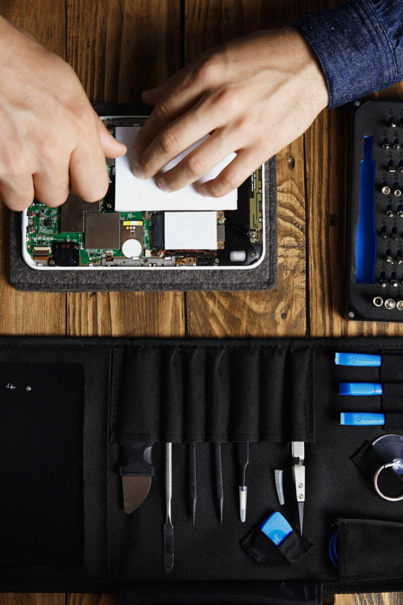 Top view hands works on broken electronic gadget to fix it near tool bag and on wooden table in service shop